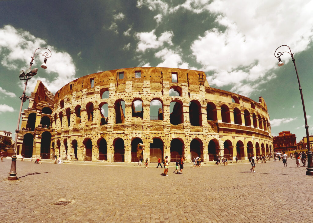 Colosseum in Rome, Italy, with tourists exploring the historical site, showcasing the ancient architecture against a blue sky.